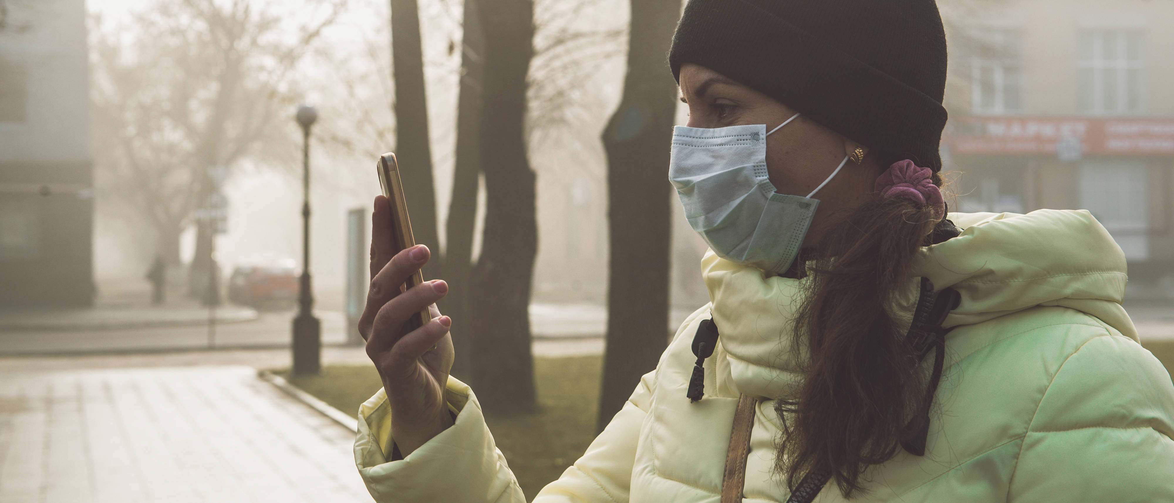 Women in an urban park, wears a face mask and looks at her phone