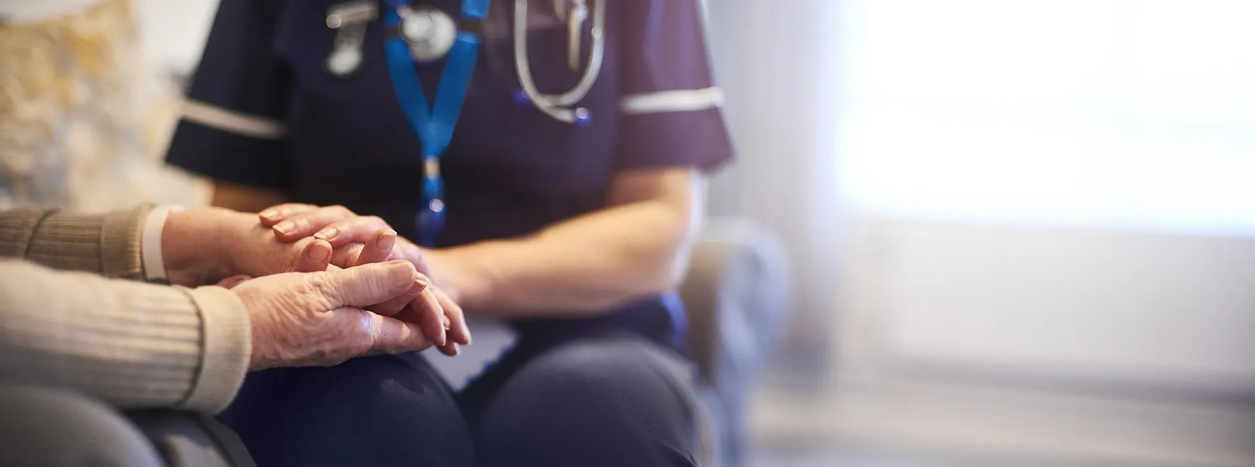 A caring moment between a care home resident and care worker, the pair holding hands