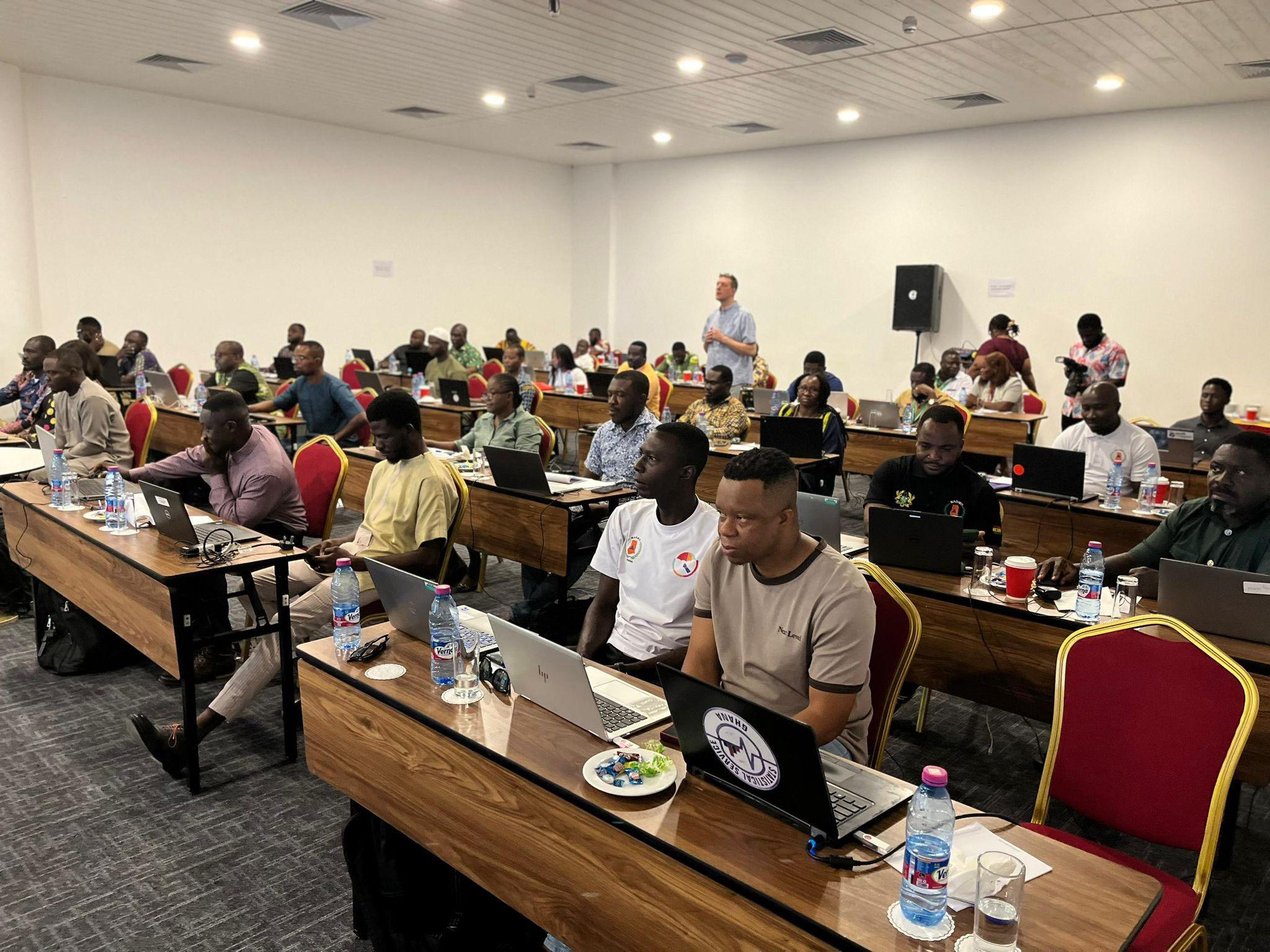 A busy room of people sitting at desks watching a presentation.