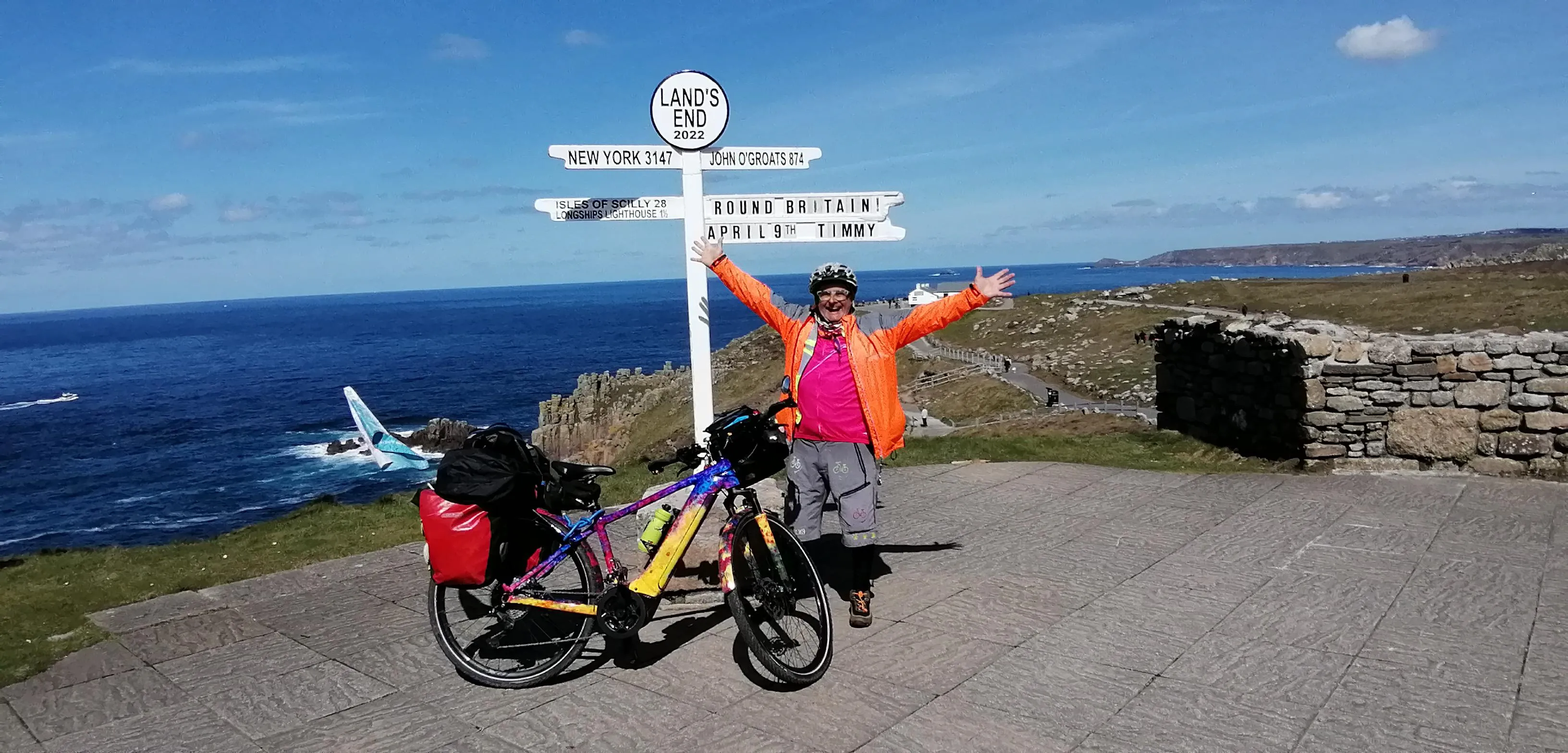 Timmy Mallett standing in front of the Land's End signpost with his bike.