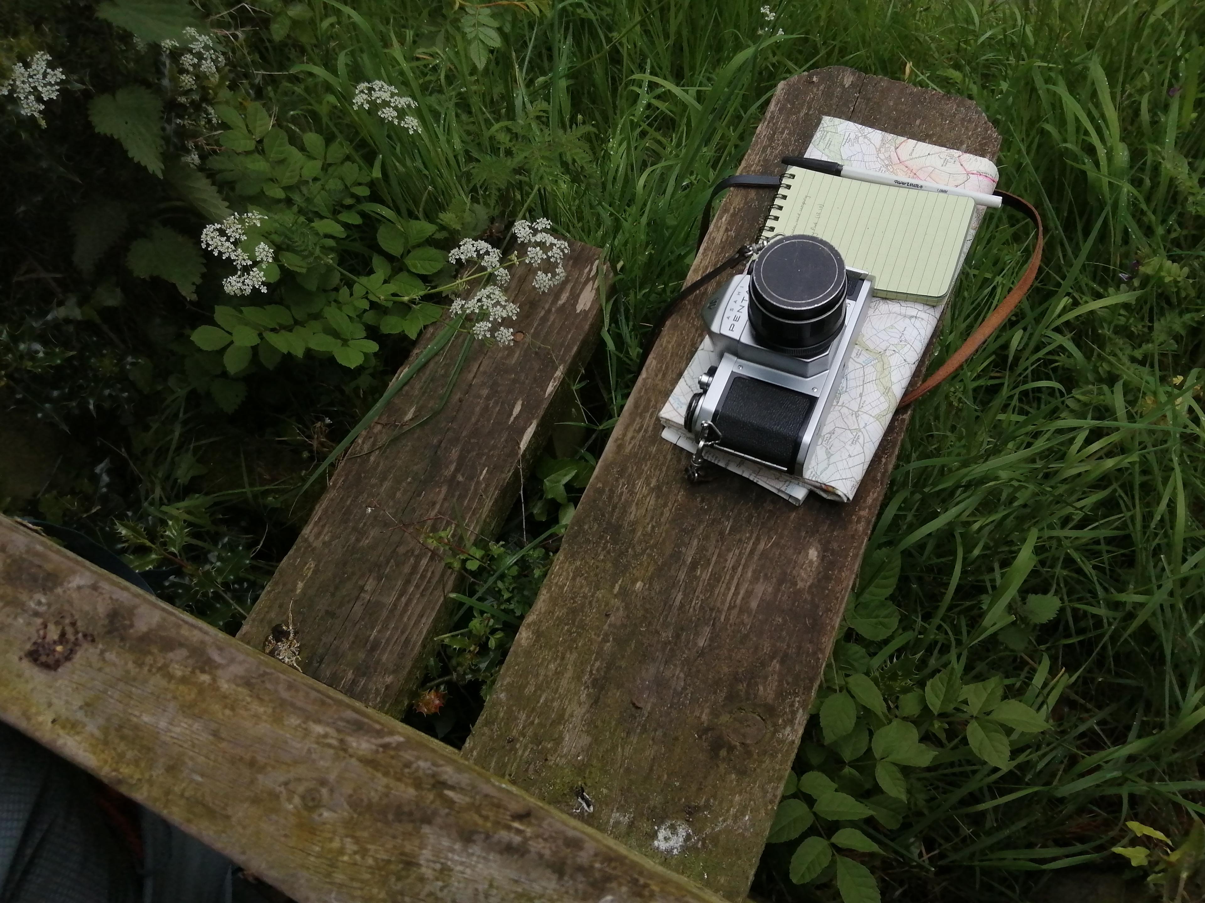 Camera, maps and notepad on a wooden stile